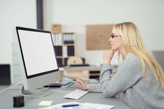 Eine blonde Frau sitzt nachdenklich vor einem Computerbildschirm.